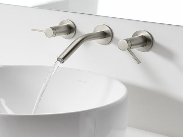 Modern bathroom sink fixtures made of brushed nickel with water pouring from the faucet into a large, detached porcelain sink bowl