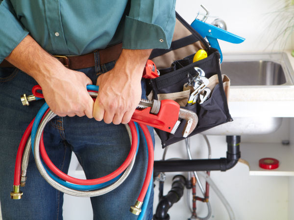 Close-up of a man holding plumbing hoses with a utility bag full of wrenches and tools on his shoulder
