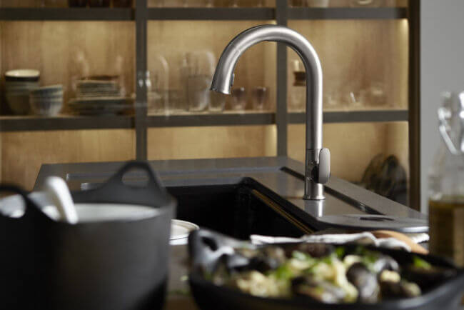 Closeup of a kitchen sink with brushed nickel finishes on a black countertop