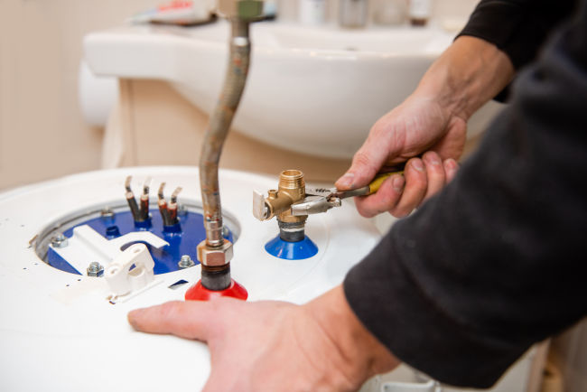 Close up on a pair of hands performing maintenance on a water heater
